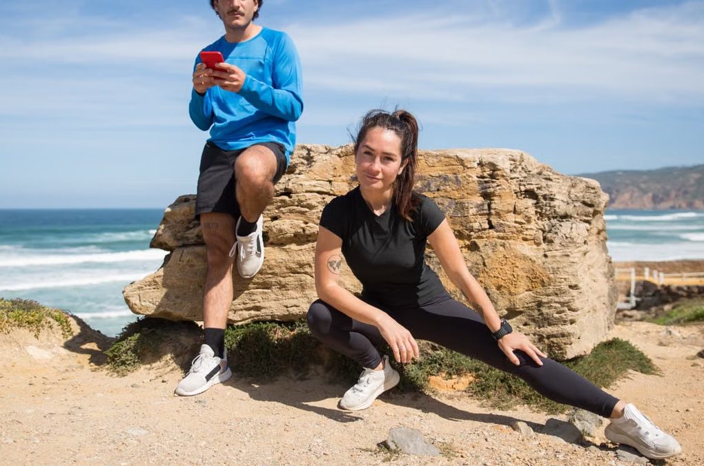 A couple stretching and using a phone on a scenic beach in Portugal.